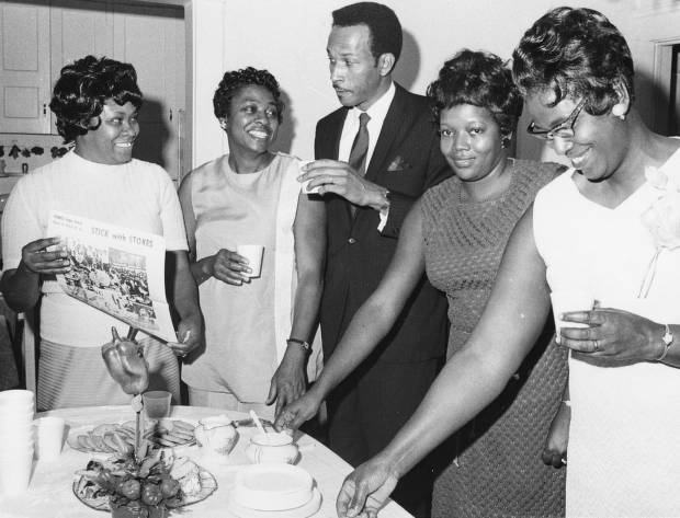 George Forbes meets with a group gathered in the home of Mrs. Marjorie Smith om East 130th Street. The woman at far left holds up printed piece, "Forbes urges every voter in ward 27 to stick with Stokes."