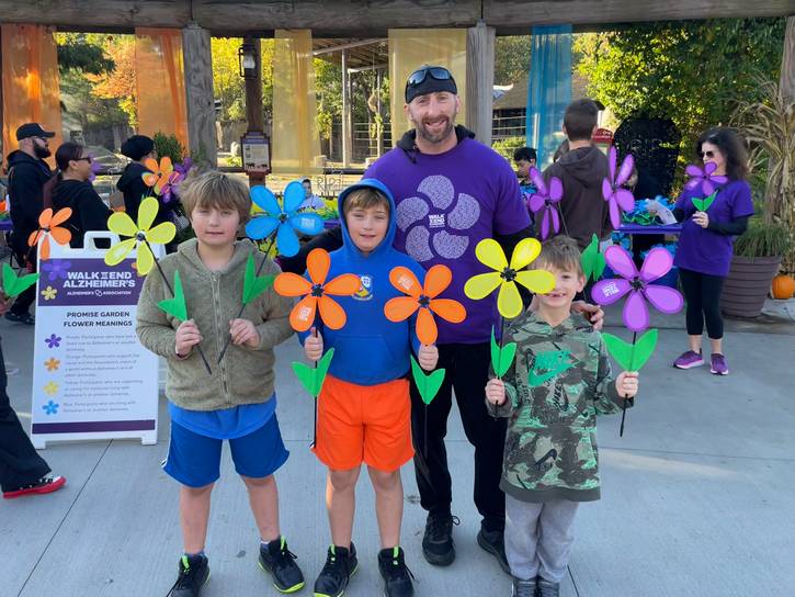 A family carries symbolic colored flowers: Blue for people living with Alzheimer's or dementia; Yellow for caregivers; Purple in memory of someone lost to the disease; Orange for advocates or general supporters.