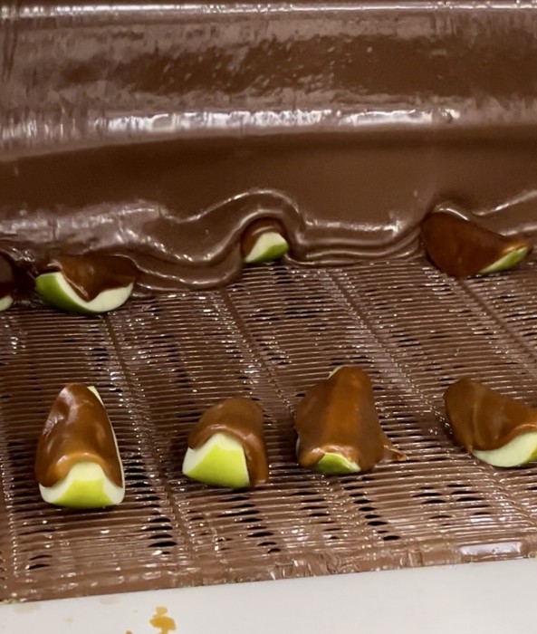 The caramel apples are coated with Malley's milk chocolate on the conveyor belt.