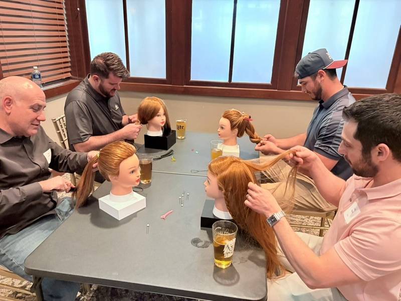 Dads practice braiding hair on mannequin heads at a Pints and Ponytails practice.