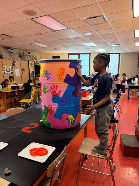 A student stands on chair to complete the rain barrel painting.