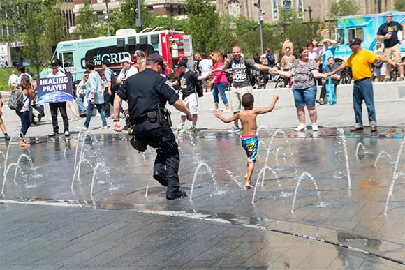 An Indiana officer runs with a local child through the fountain in Public Square